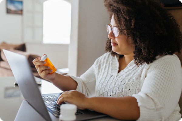 woman on laptop looking at medication bottle